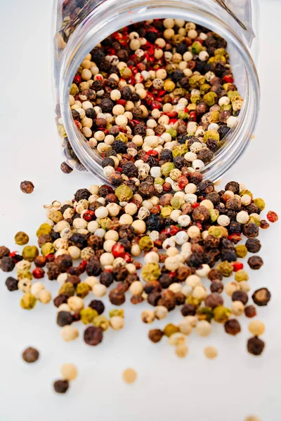 A mixture of peppers is scattered from a jar on a white background. — Stock Photo, Image