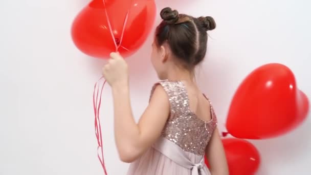 Adolescente chica danzas, risas con rojo bolas de corazones cerca de blanco pared — Vídeos de Stock