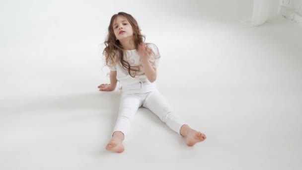 Hermosa niña con el pelo largo en ropa blanca se sienta en el suelo. — Vídeos de Stock