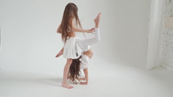 Kleine Mädchen mit langen Haaren in weißen Kleidern spielen, frönen, machen akrobatische Kunststücke — Stockvideo