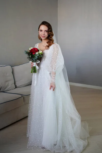 Mariée aux cheveux longs, avec bouquet de fleurs, en robe de mariée blanche dans la chambre. — Photo