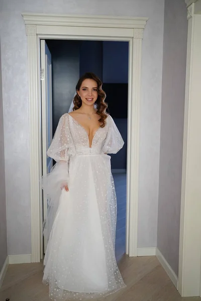 Mireasă frumoasă cu păr lung într-o rochie albă elegantă stă în ușă . — Fotografie, imagine de stoc