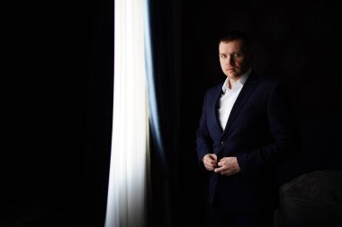 Karanlık bir odada, pencerenin yanında ceketli bir adam..