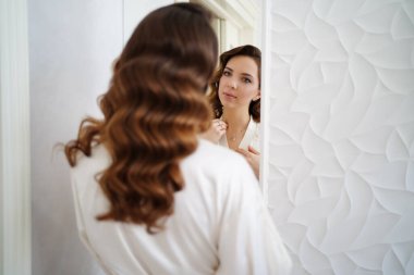 İpek bornozlu gelin aynaya bakar ve boynundaki kolyeyi düzeltir