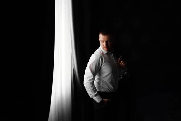 在一间黑暗的房间里，穿着白衬衫的男人站在窗边. — 图库照片