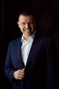 Karanlık bir odada ceketli gülümseyen bir adamın portresi..