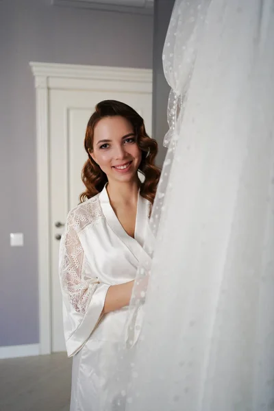 Наречена з довгим волоссям у шовковому халаті біля білої весільної сукні — стокове фото