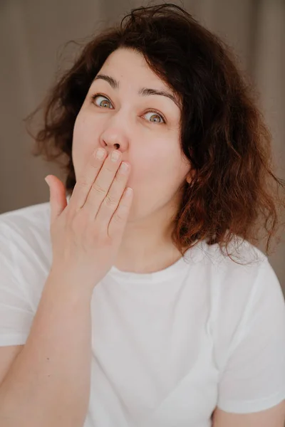 Retrato de una mujer morena sorprendida con el pelo rizado en una camiseta blanca. — Foto de Stock