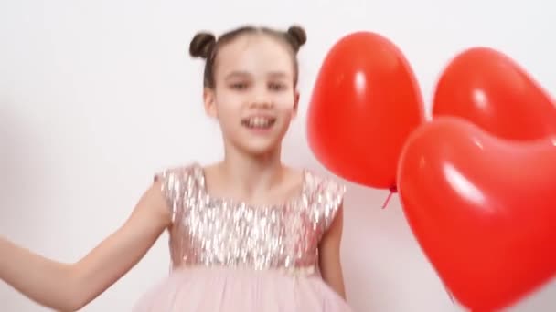 Menina adolescente dança, ri com bolas vermelhas de corações perto da parede branca — Vídeo de Stock