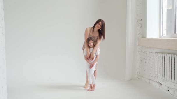 Mamá y su hija posan en un estudio de fotografía en blanco para una sesión de fotos. tras bastidores. — Vídeos de Stock