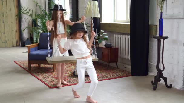 Duas belas meninas passeios em chapéus pretos em um balanço no sótão. — Vídeo de Stock