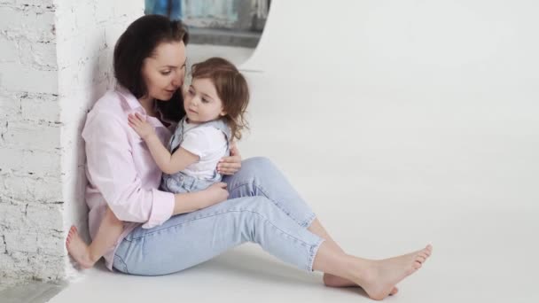 Güzel, mutlu bir aile yerde oturup beyaz fotoğraf stüdyosunda sarılır. sahne arkası. — Stok video