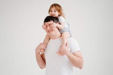 Küçük kız babasının omuzlarında oturur ve elleriyle gözlerini kapatır.