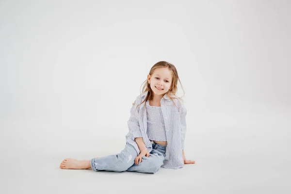 Liten flicka med långt hår i jeans och skjorta poserar mot en vit bakgrund. — Stockfoto