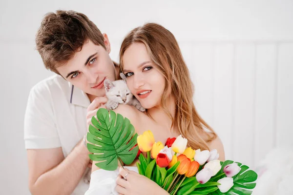 Un hombre le dio a su amada mujer un ramo de tulipanes coloridos y un gatito blanco. — Foto de Stock