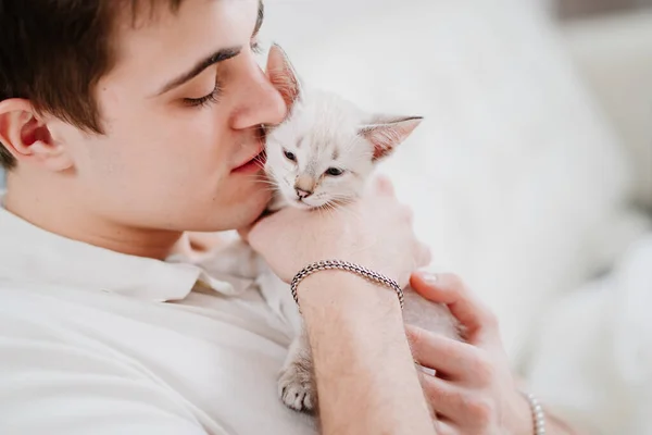젊은 남자가 작은 흰 고양이를 안고 그를쓰다듬는다. nevsky masquerade cat. — 스톡 사진