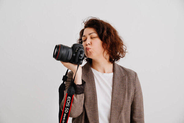 brunette woman in a checkered jacket on a white background kisses camera in hand