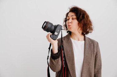 Kareli ceketli esmer kadın beyaz arka planda kamerayı öpüyor.