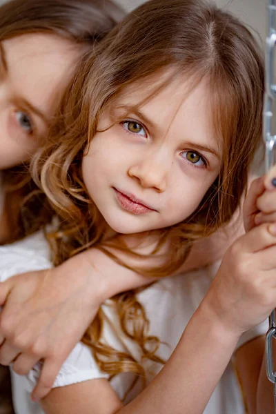 Zamknij się. dziewczyna w białych ubraniach jeździ na huśtawce. starsza siostra przytula młodszą — Zdjęcie stockowe