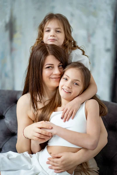 Maman sur le canapé câline avec ses filles. famille heureuse. — Photo