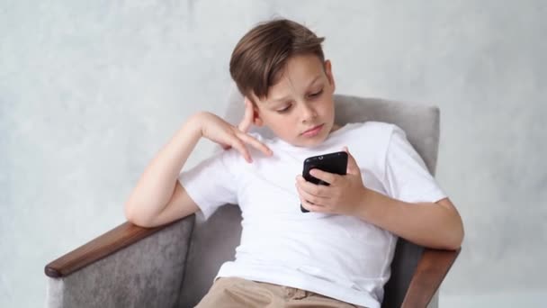 Un adolescente con una camiseta blanca con un smartphone en la mano. — Vídeo de stock