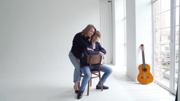 Una madre con su hijo en ropa azul posa en una silla por ventana para una sesión de fotos — Vídeo de stock