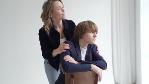 Мати з сином у блакитному одязі позує на стілець за вікном для фотосесії — стокове відео