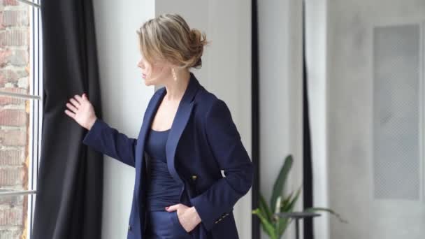 Una mujer rubia con un traje azul posa mirando por la ventana en un estudio fotográfico. — Vídeo de stock