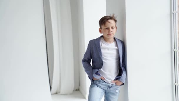 A teenage boy in a jacket and jeans poses standing by a window. — Stock Video