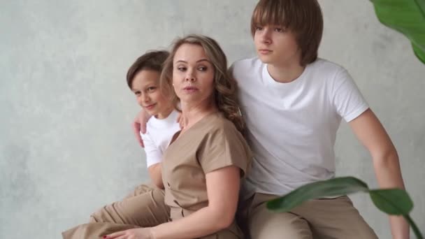 Matka i synowie w beżowych i białych ubraniach pozują na krześle na sesję zdjęciową — Wideo stockowe