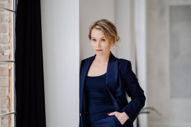 Mavi takım elbiseli sarışın kadın fotoğraf stüdyosunda poz veriyor. İş kadını