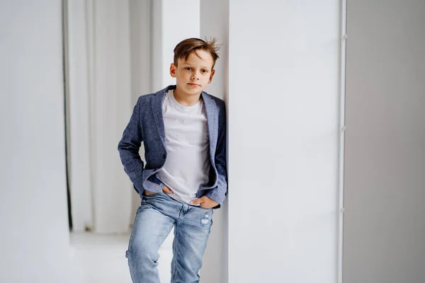 En tonårspojke i jacka och jeans poserar vid ett fönster. — Stockfoto