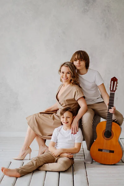 Mère et fils en vêtements beige et blanc posent pour la séance photo. jouer de la guitare — Photo