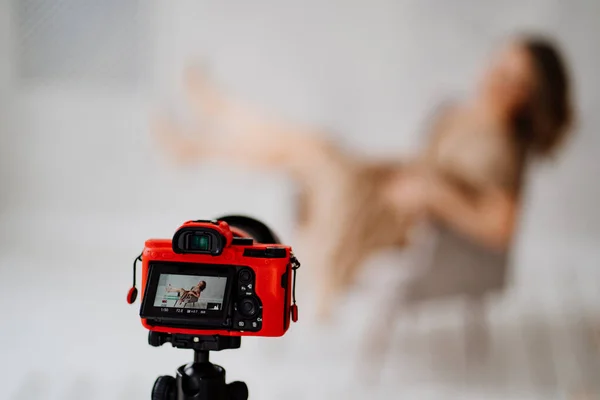Kameraya odaklan. Bej elbiseli bir kadın fotoğraf stüdyosunda gri bir sandalyede poz veriyor.. — Stok fotoğraf