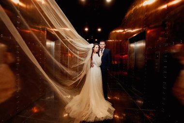 Gelin ve damat zarif bir elbise içinde, karanlık bir koridorda duvağı var.