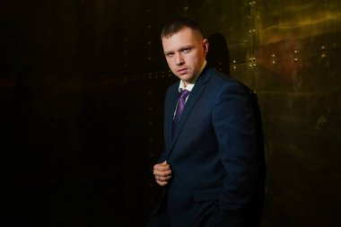 Koyu mavi takım elbiseli bir adam metal bir duvarın karşısında duruyor. Bir iş adamının portresi