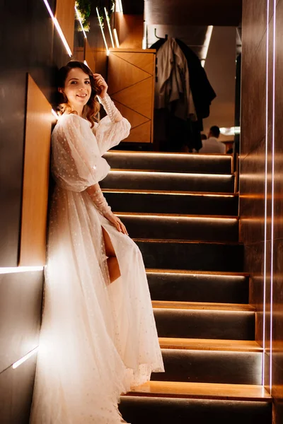 Невеста в белом платье стоит на плохо освещенной лестнице — стоковое фото