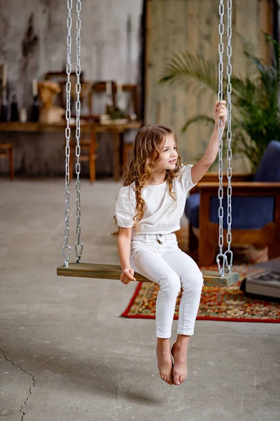 Chica bonita en ropa blanca paseos en columpio. habitación original de los niños — Foto de Stock