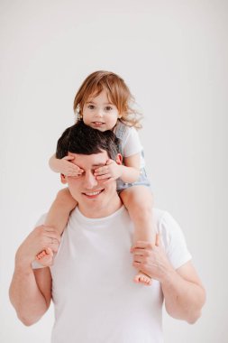 Küçük kız babasının omuzlarında oturur ve elleriyle gözlerini kapatır.