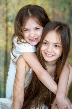 Beyaz elbiseli, uzun saçlı iki küçük kız sarılıyor. Kardeşler arasındaki aşk. 