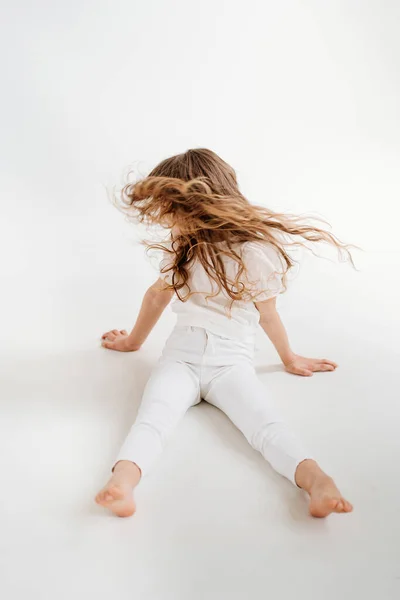 Niña con el pelo largo se sienta en el suelo, y agitando la cabeza, el pelo está volando — Foto de Stock