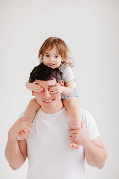Pequena filha senta-se sobre os ombros de seus pais e fecha os olhos com as mãos — Fotografia de Stock