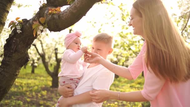 Ευτυχισμένη μαμά με γιο και κόρη στον ανοιξιάτικο ανθισμένο κήπο. κλεφτοχείλια — Αρχείο Βίντεο