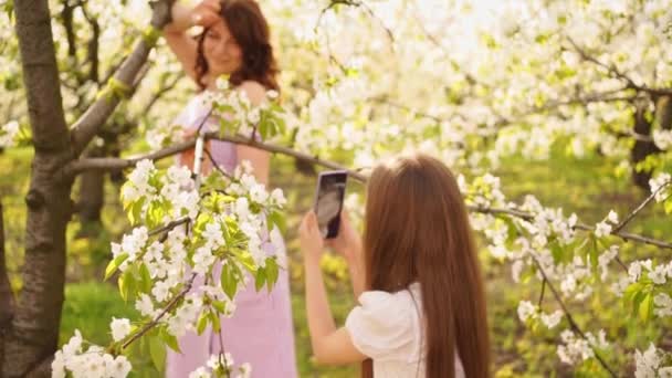 Filha tira fotos em suas mães telefone no jardim florido. — Vídeo de Stock