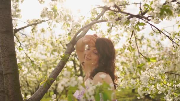 Приваблива жінка біля квіткового дерева в весняному парку. Вишневий сад. Сонячний блиск — стокове відео