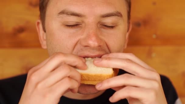 Een man bijt en eet een broodje van wit brood. — Stockvideo