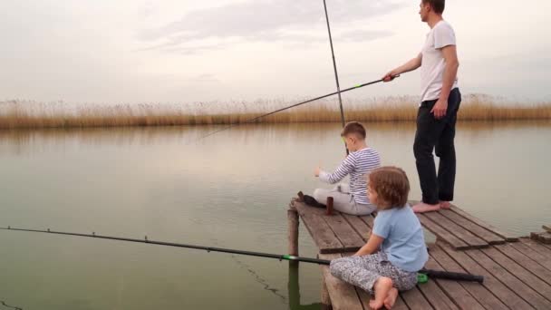 Vater und Sohn und Tochter auf einer Holzbrücke fangen Fische aus dem Fluss. — Stockvideo