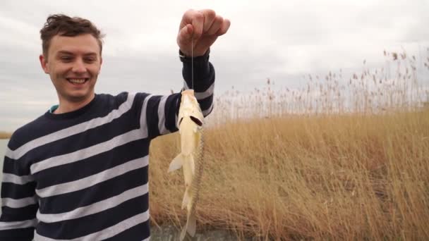 Ένας άντρας κρατάει ένα ψάρι που πιάστηκε σε καλάμι ψαρέματος. ψαράς. — Αρχείο Βίντεο