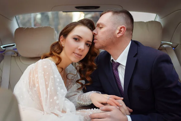 Das Brautpaar auf dem Rücksitz des Autos. Ein Auto für eine Hochzeit mieten. — Stockfoto