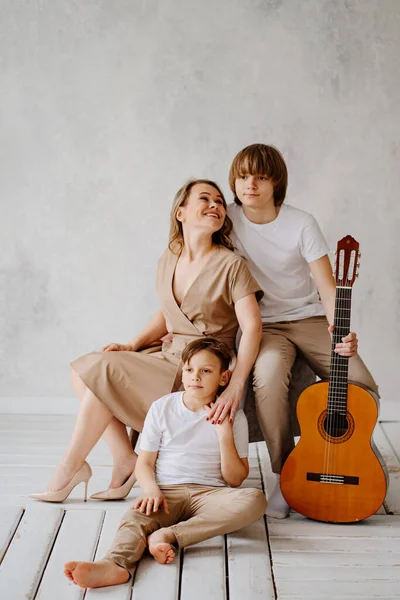 Mère et fils en vêtements beige et blanc posent pour la séance photo. jouer de la guitare — Photo